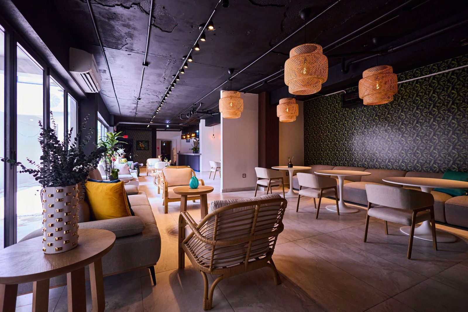 Lounge at Ola Boutique Hotel with round tables, rattan chairs, pendant lamps and a tropical patterned wall