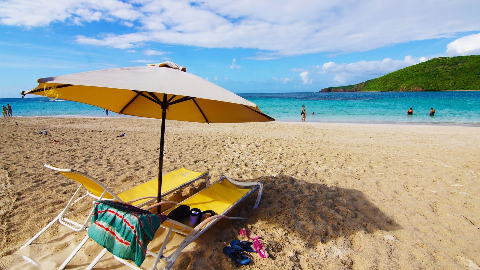 Yellow beach umbrella and loungers on golden sand beside turquoise water in Puerto Rico