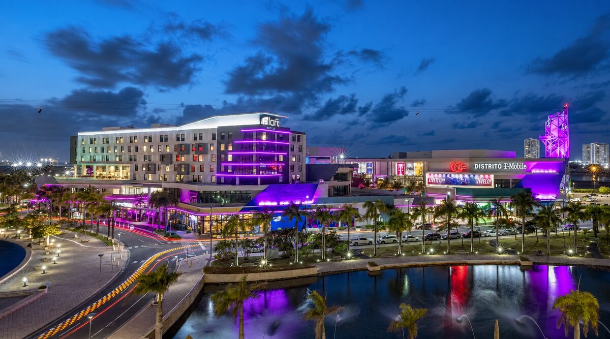 DISTRITO T-Mobile in San Juan at dusk, with the illuminated sign, entertainment tower, palms and reflecting water