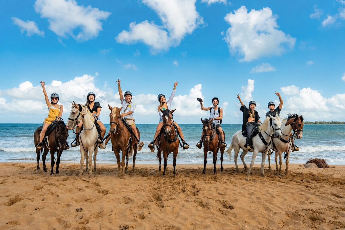Seven riders on horseback lined up along the sand at the water's edge on a sunny beach in Luquillo, Puerto Rico